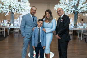 Family posing with the venue owner during a beautifully decorated baptism celebration at Oasis Convention Centre, featuring illuminated floral trees in the background.