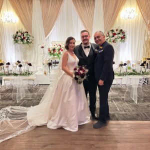 Bride and groom posing with the venue host inside an elegant floral wedding setup at Oasis Convention Centre.